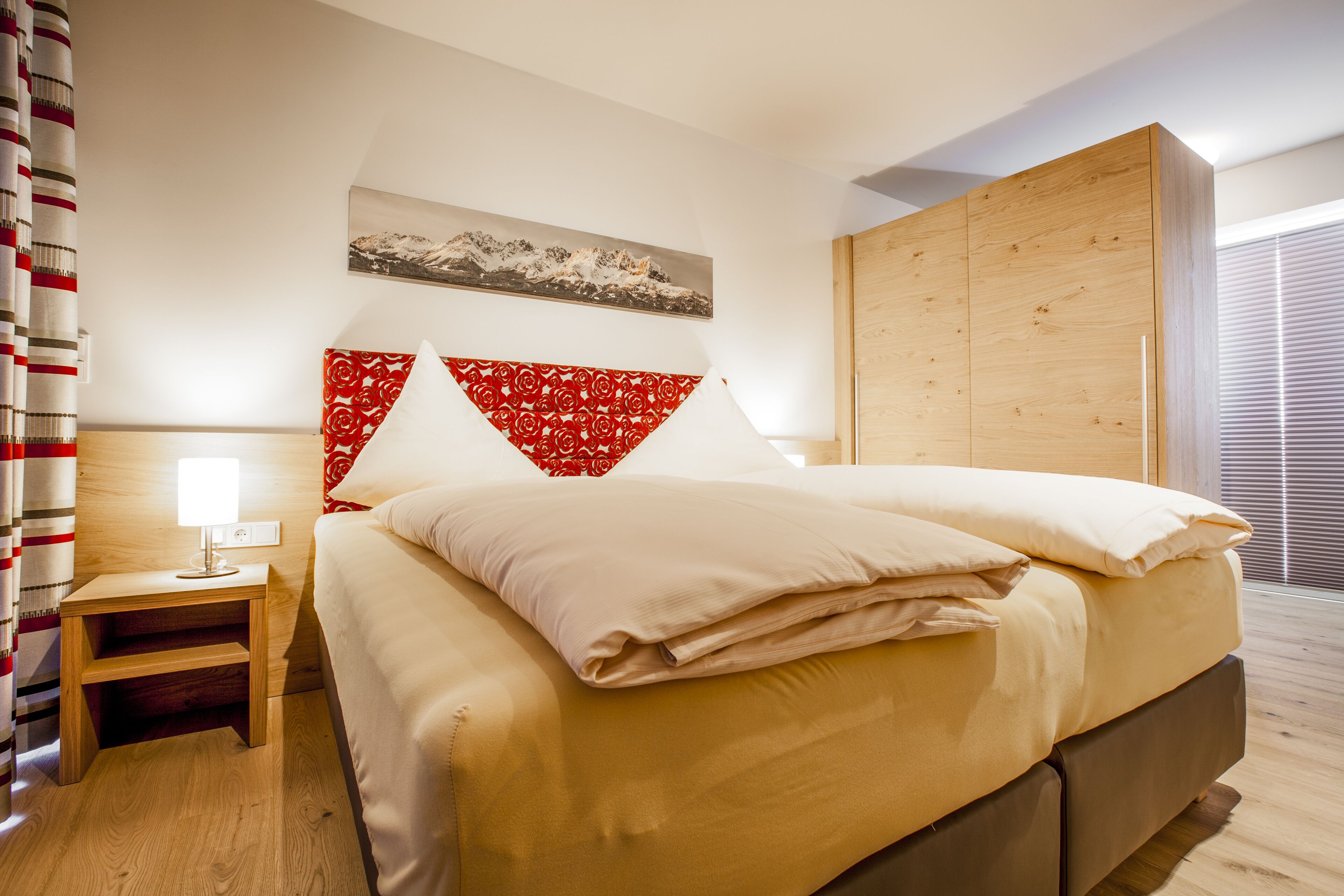 Habitación de hotel con cama, mesita de noche, armario de madera y ventana con persianas.