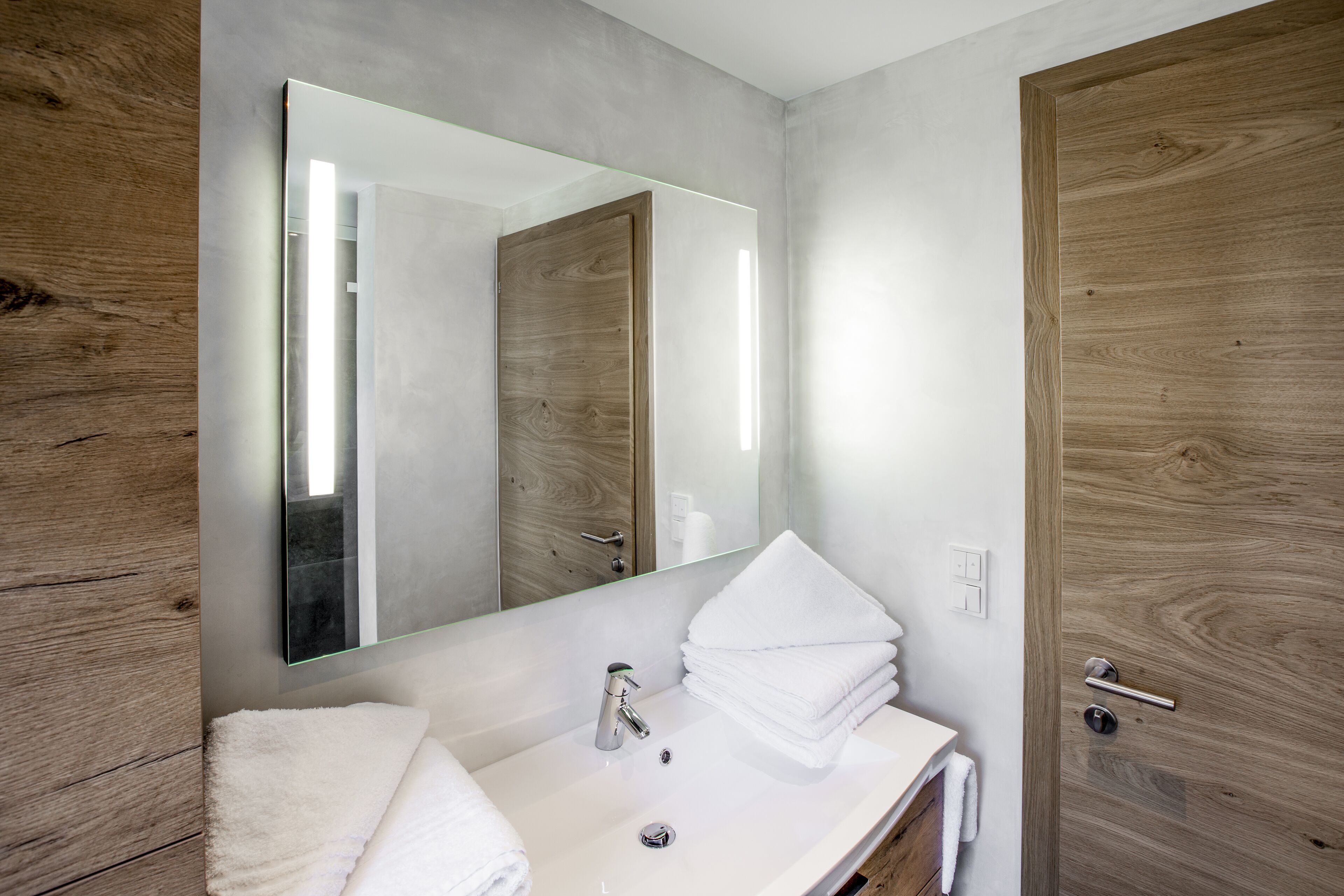 A bathroom with a wooden vanity, a white sink, a mirror, and a towel rack.