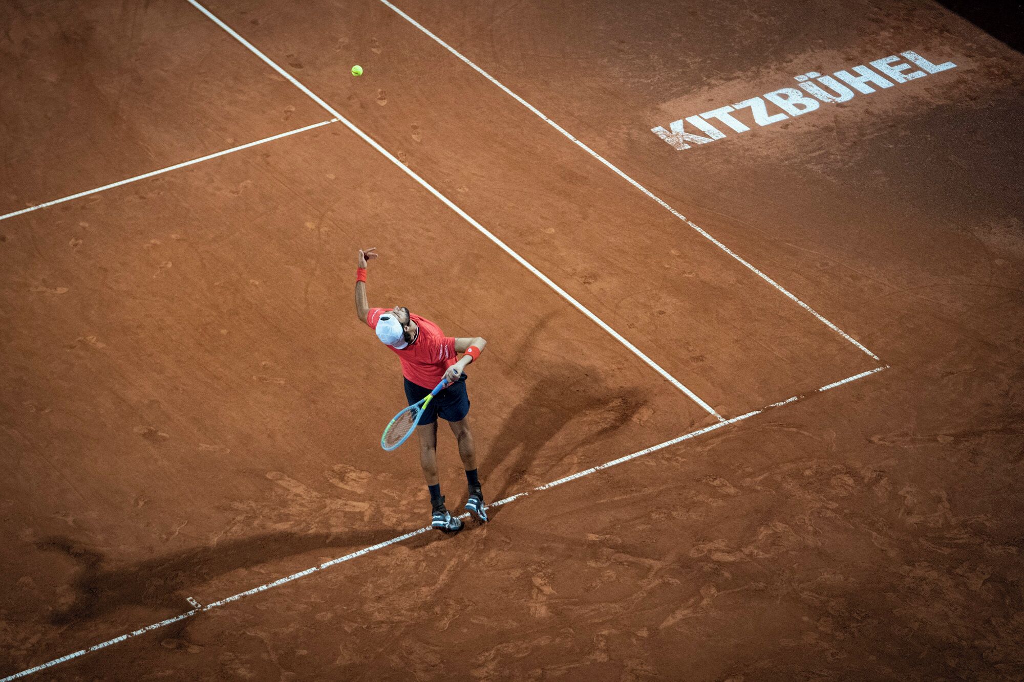 A tennis player on a clay court with "MITZBUHEL" written on the surface.
