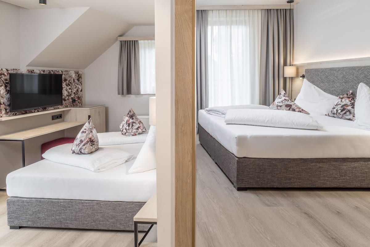 Quarto de hotel moderno com televisão de ecrã plano, secretária, cama com almofadas florais e uma grande janela com cortinas.