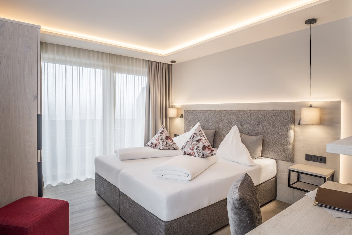 Quarto de hotel moderno com uma cama grande, mesas de cabeceira, uma escrivaninha e um banquinho vermelho.