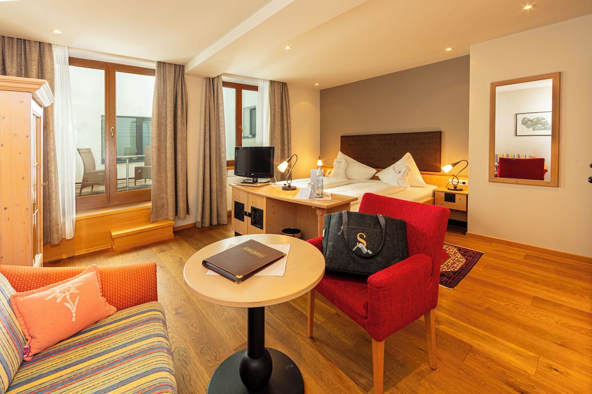 Quarto de hotel com cama, escrivaninha, cadeira, sofá e janela com cortinas.