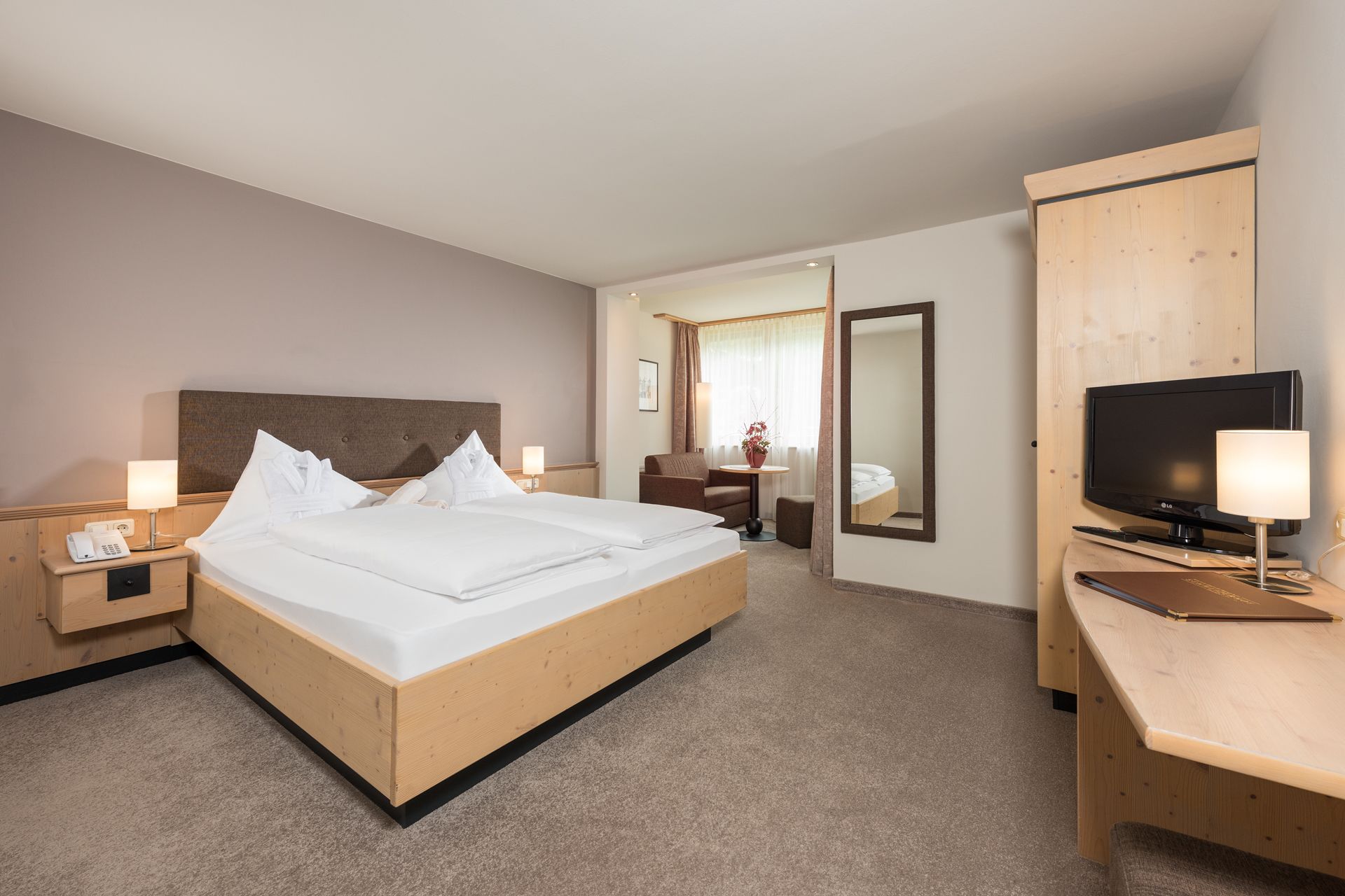 Ein Hotelzimmer mit Bett, Nachttisch mit Telefon, Schreibtisch mit Fernseher und Spiegel.