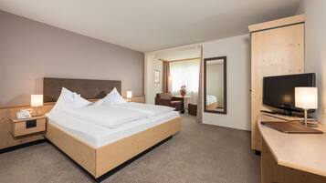 A hotel room with a bed, bedside table with a phone, a desk with a TV, and a mirror.