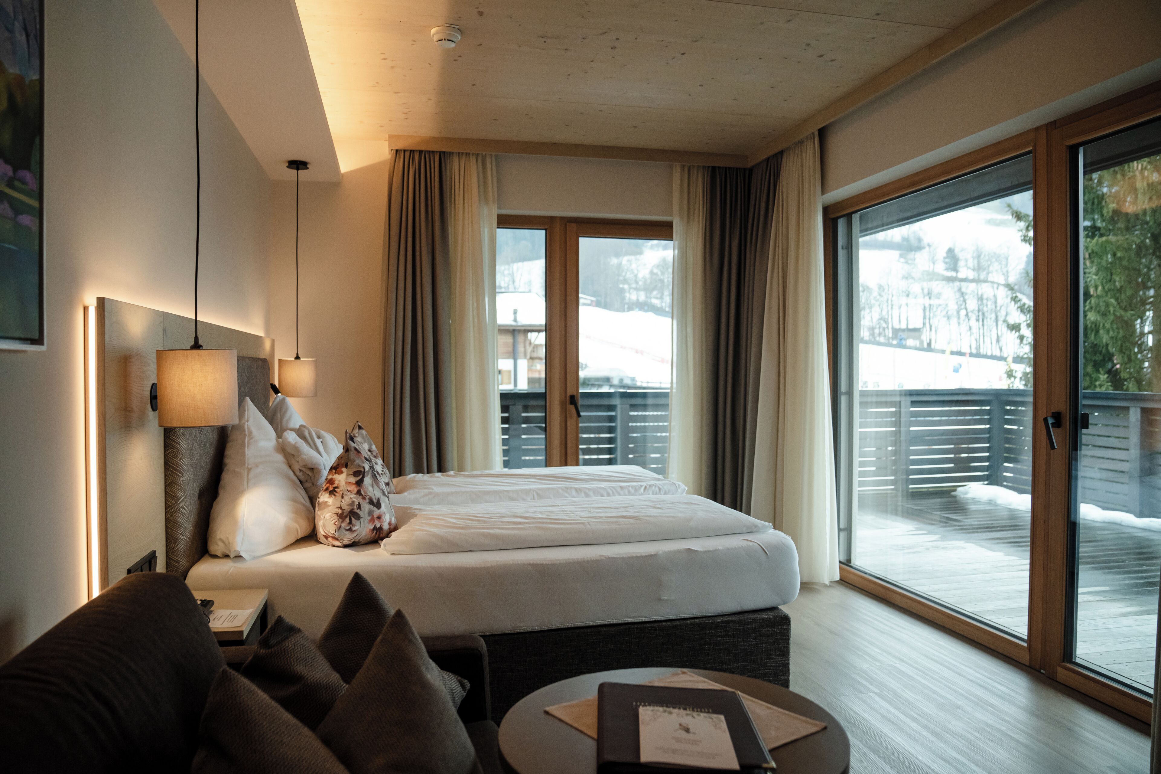 Ein Hotelzimmer mit Bett, einer Couch, einem kleinen Tisch und Blick auf eine verschneite Landschaft durch das Fenster.