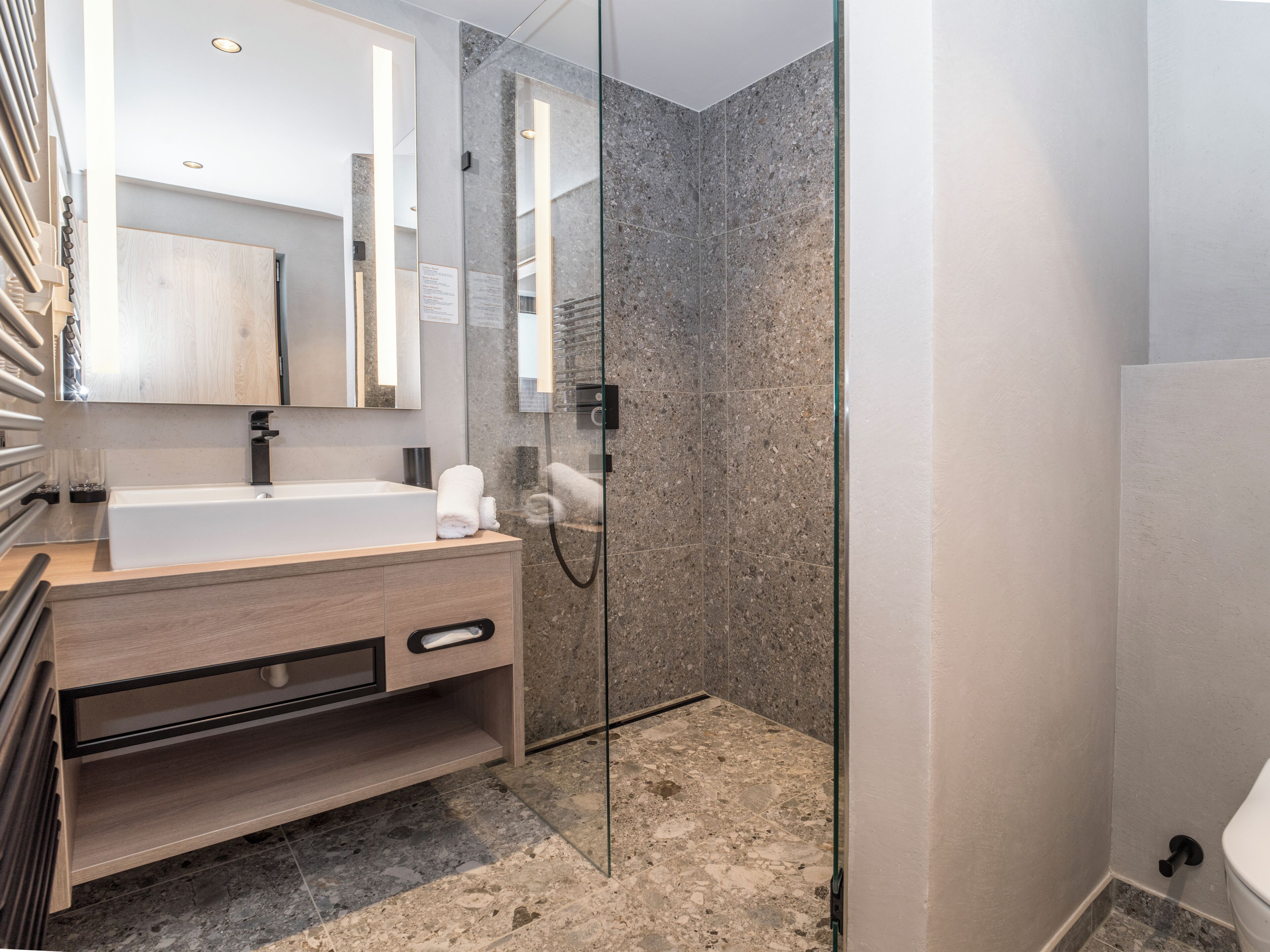 Un baño moderno con ducha envuelta en vidrio, tocador de madera y un espejo grande.