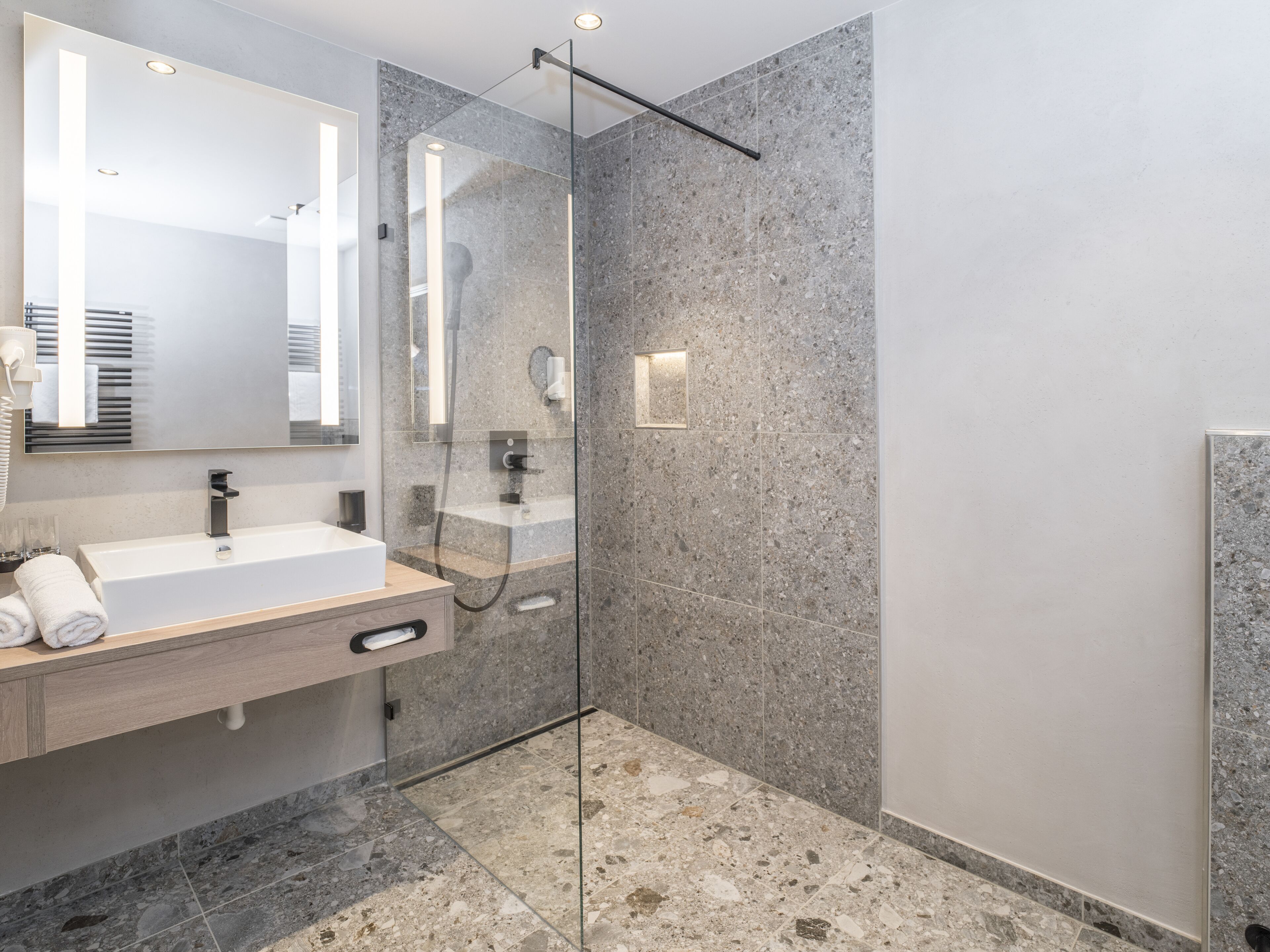 A modern bathroom with a glass-enclosed shower, a large mirror, and a white sink.