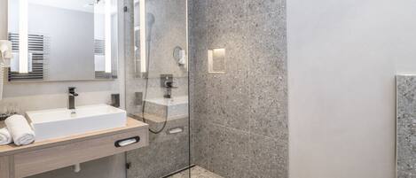 A modern bathroom with a glass-enclosed shower, a large mirror, and a white sink.