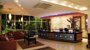 A modern hotel lobby with a reception desk, sofas, and a large window overlooking greenery.