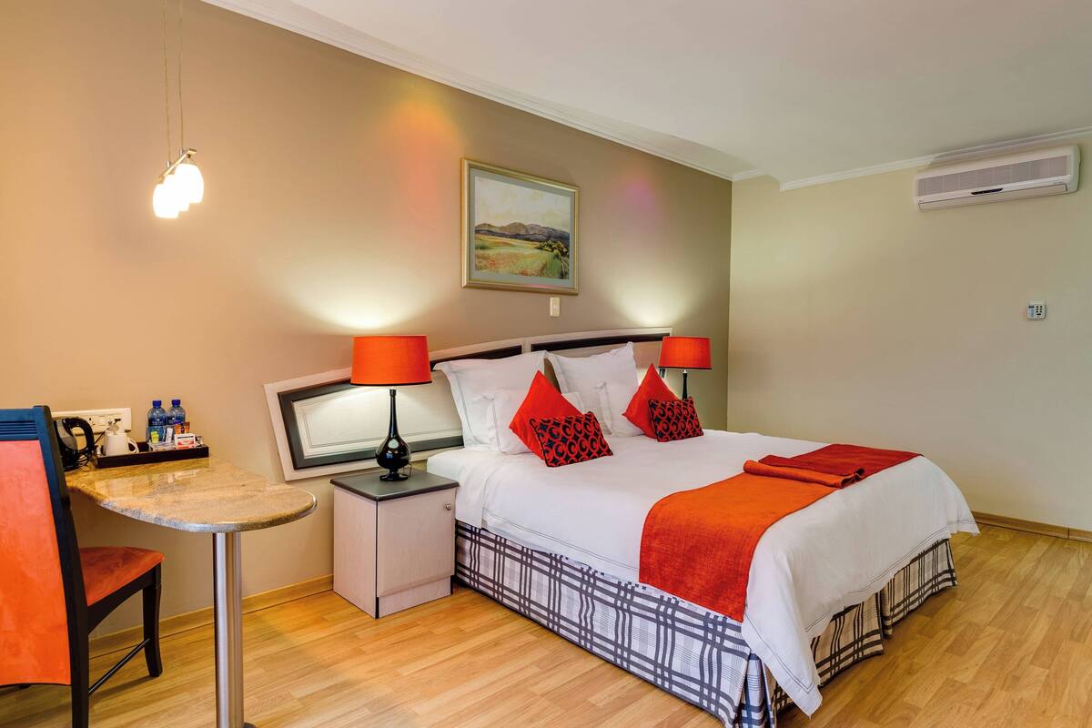 A hotel room with a bed, a desk, a chair, and a painting on the wall.