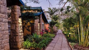 A pathway flanked by stone pillars and lush tropical plants, leading to a building with a blue roof.