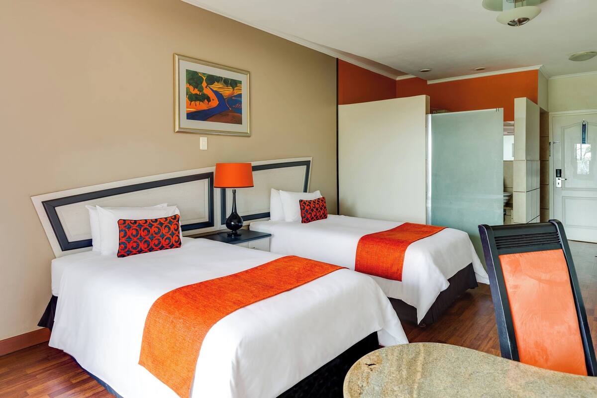 A hotel room with two beds, a painting on the wall, and a refrigerator.