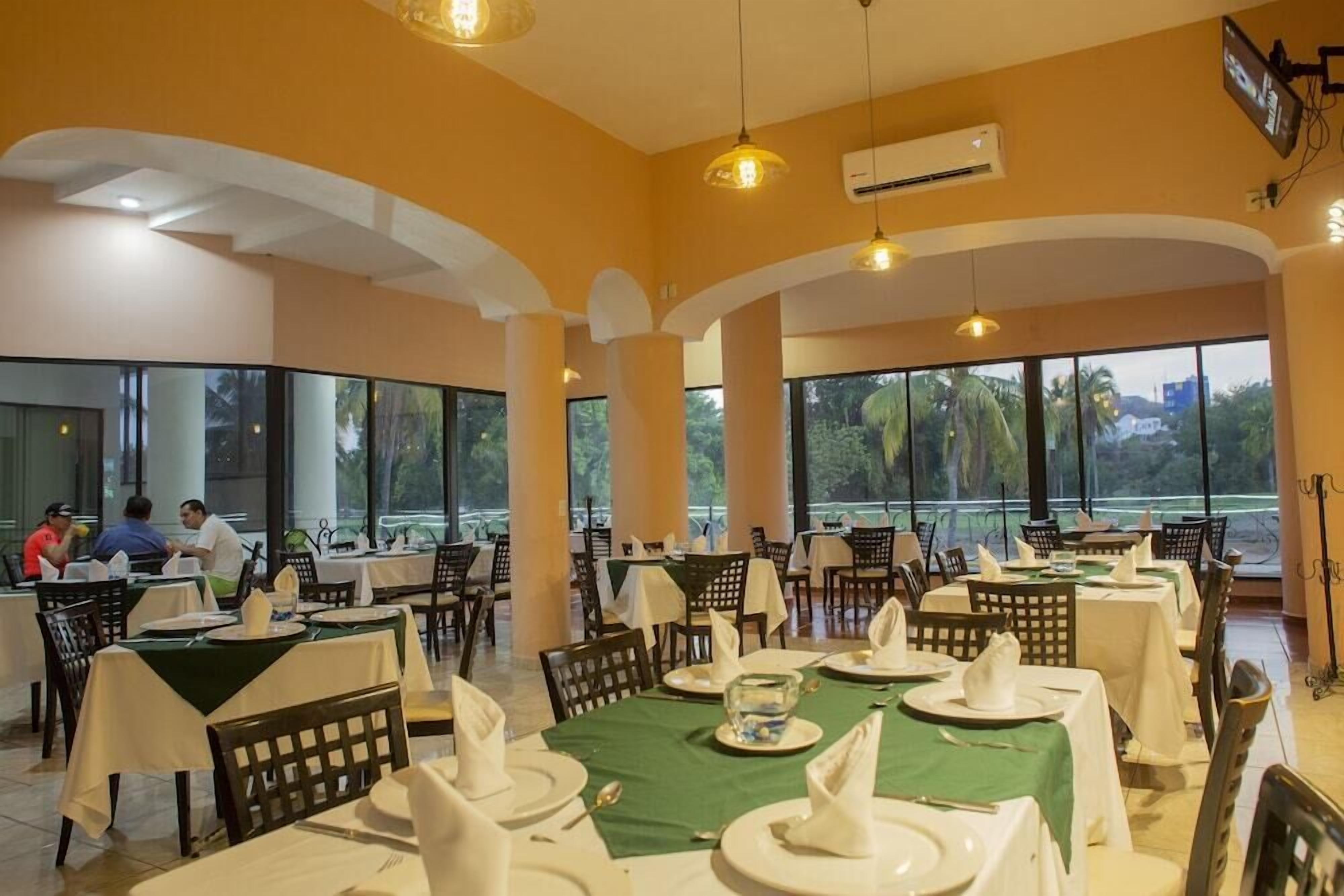 Un restaurante con mesas listas para comer, amplias ventanas y un equipo de aire acondicionado en la pared.