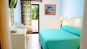 A bedroom with a bed, a desk, and a chair. There is a window with curtains, a painting on the wall, and a lamp on the bedside table. - Costa Brava (Manzanillo)