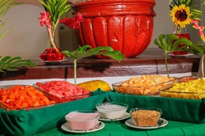 Una mesa de buffet con diversos alimentos y una olla roja grande al fondo.