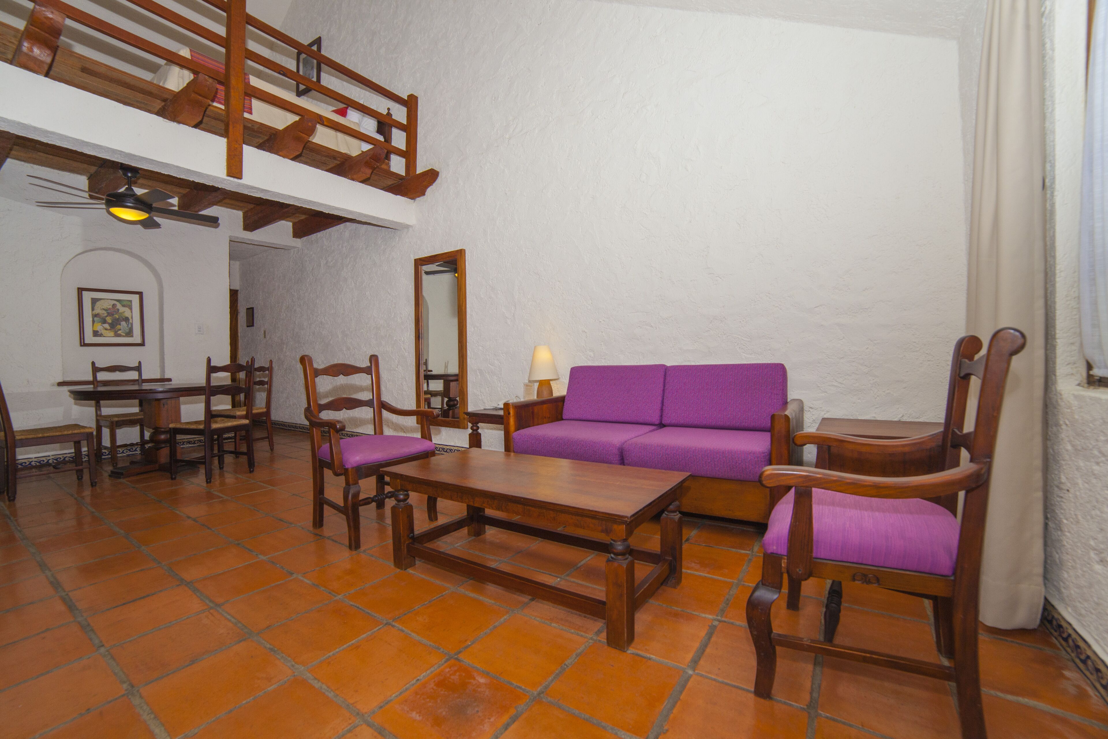 Una sala de estar con un sofá púrpura, sillas de madera, una mesa de centro y un comedor con una mesa y sillas.