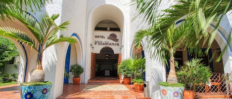 Ein Hotel Eingang mit einem Schild, auf dem 'Hotel Villablanca' steht, umgeben von Topfpflanzen und Palmen.