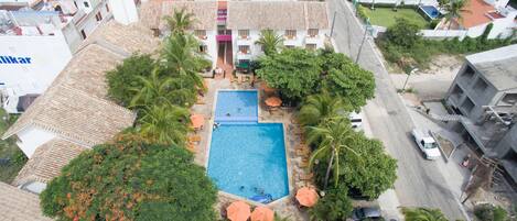 An aerial view of a residential area with a swimming pool surrounded by palm trees and a small garden.