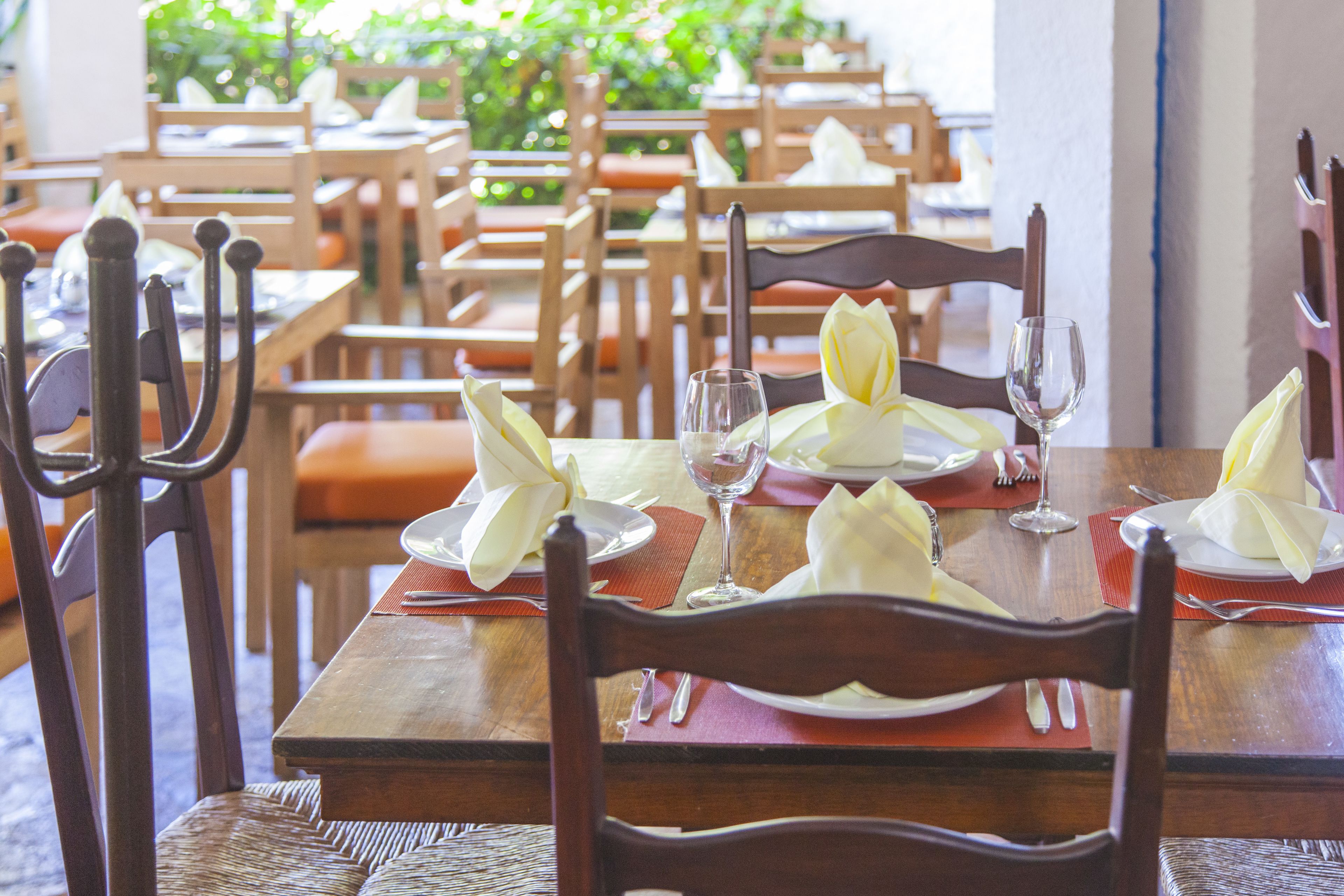 Um restaurante com mesas e cadeiras de madeira, cada conjunto com pratos, talheres e guardanapos.