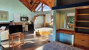 A spacious room with a large bed, a wooden ceiling, a built-in TV, a kitchen area, and a view of the outdoors. - Casa del Bosque Apart, Suites & Spa (Villa La Angostura)