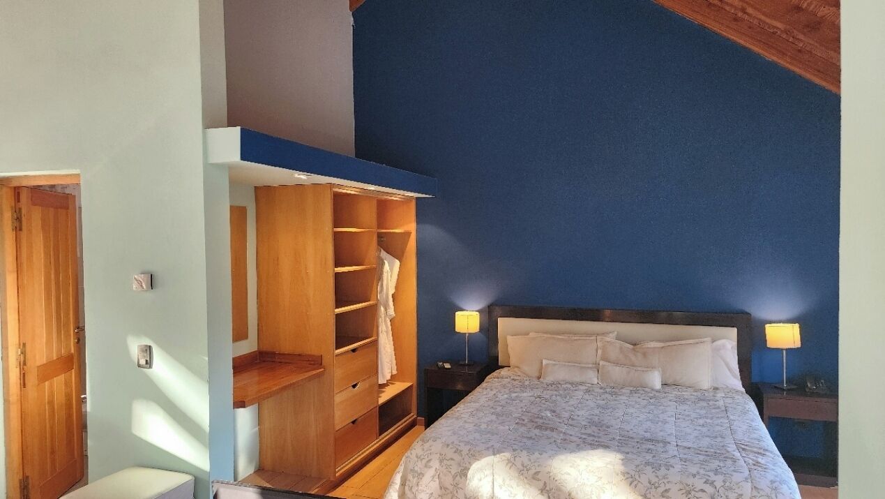 Un dormitorio con cama, lámparas de noche, un armario de madera y pared azul.