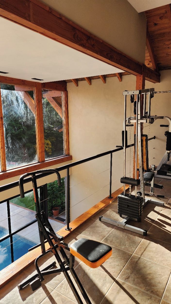 Ein Fitnessraum mit Trainingsgeräten, ein Fenster mit Blick auf Bäume und ein Balkon mit Geländer.