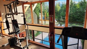 A gym with exercise equipment, large windows, and a view of a swimming pool and forest. - Casa del Bosque Apart, Suites & Spa (Villa La Angostura)