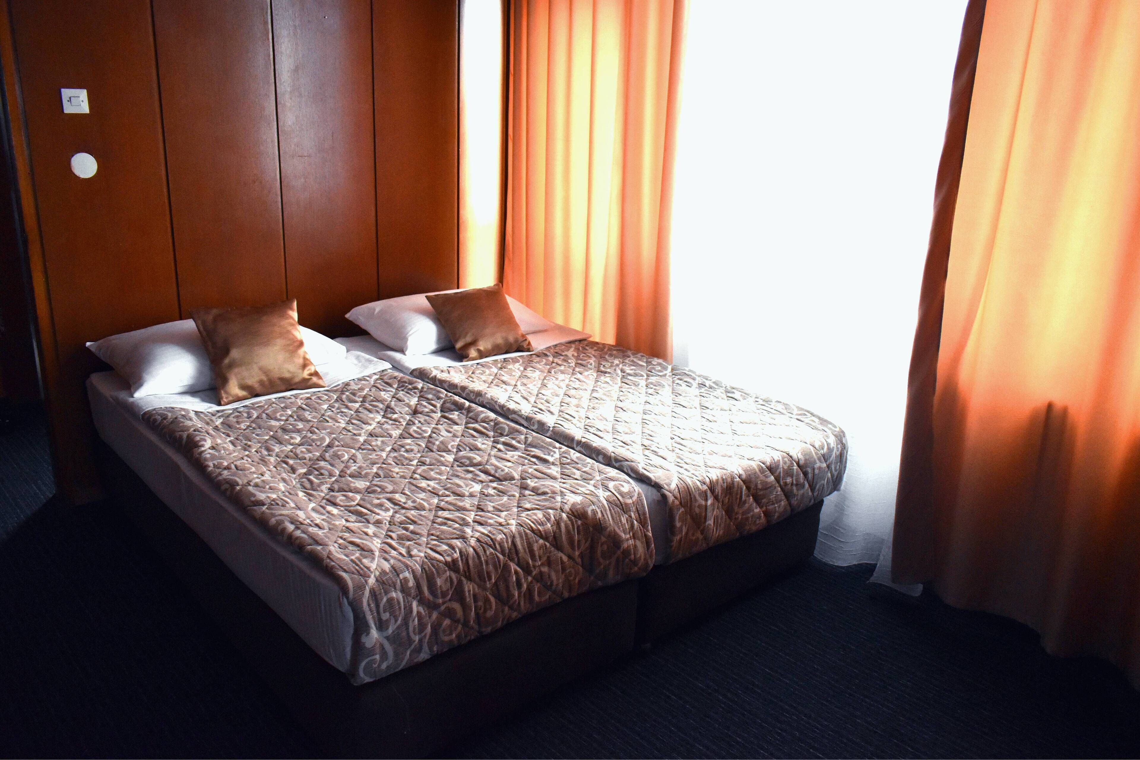 A double bed with a patterned bedspread, two pillows, and a wooden headboard in a hotel room.
