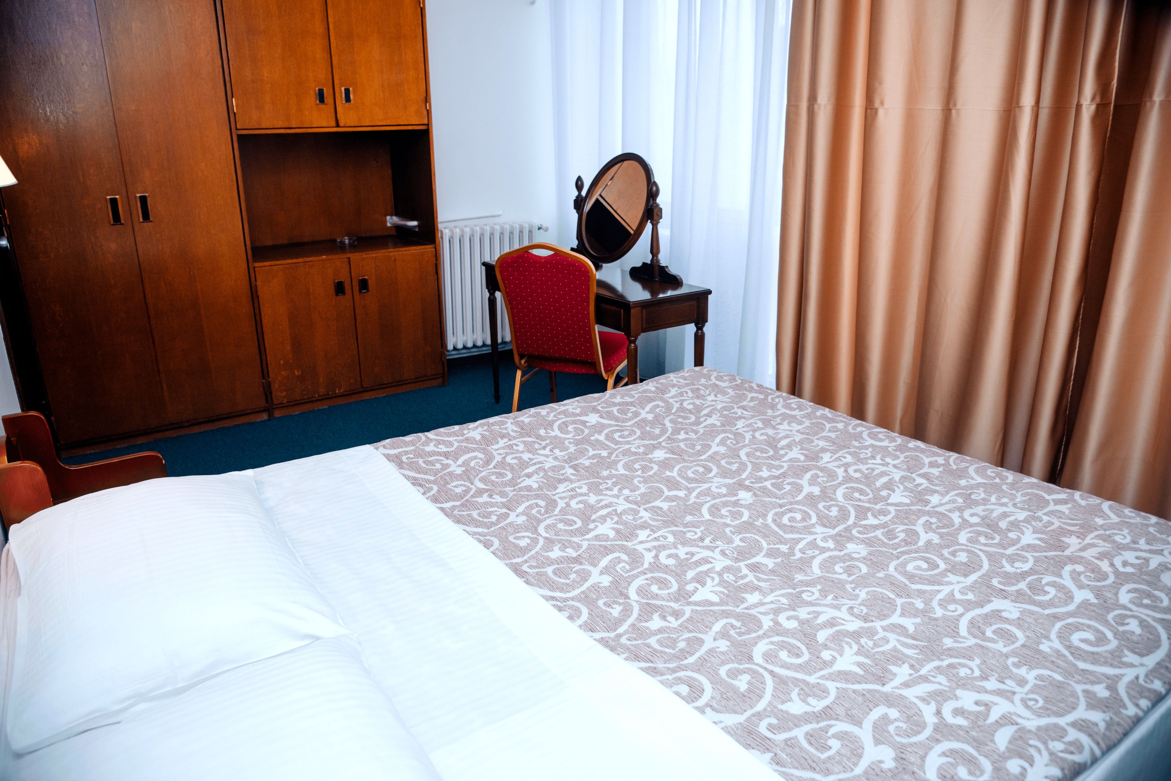 A hotel room with a bed, a desk with a mirror, a red chair, and wooden wardrobes.