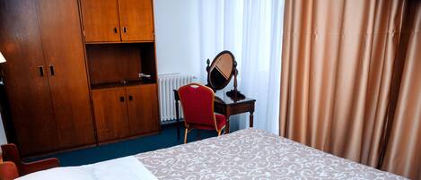 Habitación de hotel con cama, escritorio con espejo, una silla roja y armarios de madera.