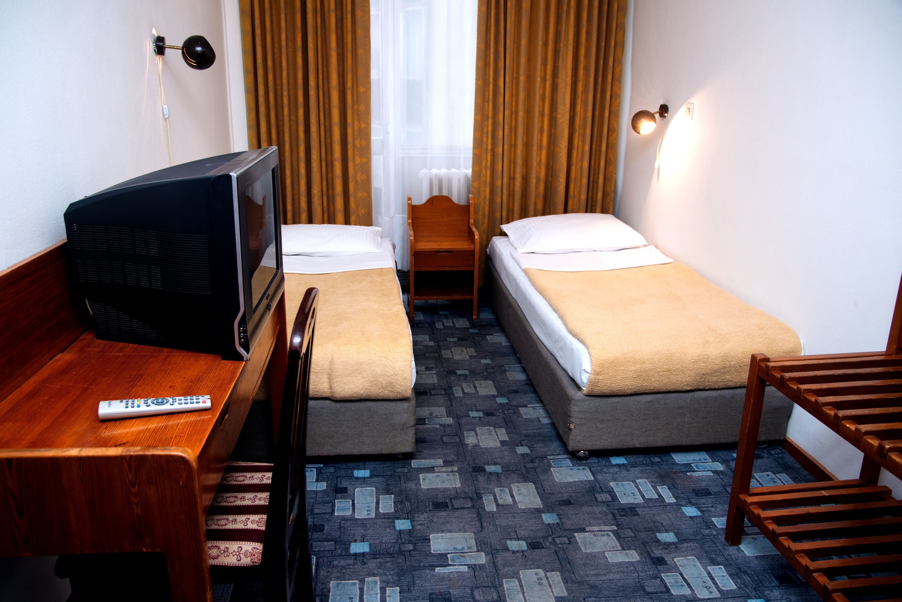 A hotel room with two single beds, a wooden desk with a TV, a chair, and a small table.