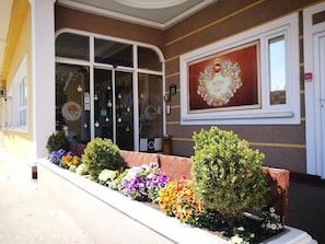 A hotel entrance with a reception desk, a sign reading "HOTEL LAV", and a flower bed with various flowers. - Hotel Lav (Belgrade)