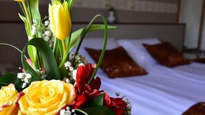 A bed with white linens and brown pillows, a bouquet of flowers including yellow tulips and red roses, and a wooden headboard. - Hotel Lav (Belgrade)