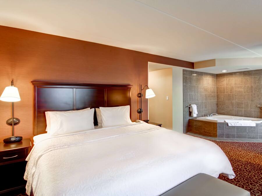 Habitación de hotel con una cama grande, lámparas de noche, una mesita de noche y un baño con bañera y zona de ducha.