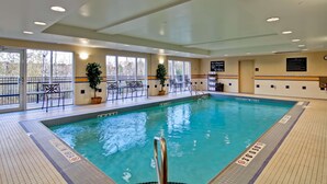 An indoor swimming pool with clear water, surrounded by windows, chairs, and potted plants. - Hampton Inn by Hilton Sudbury (Sudbury)