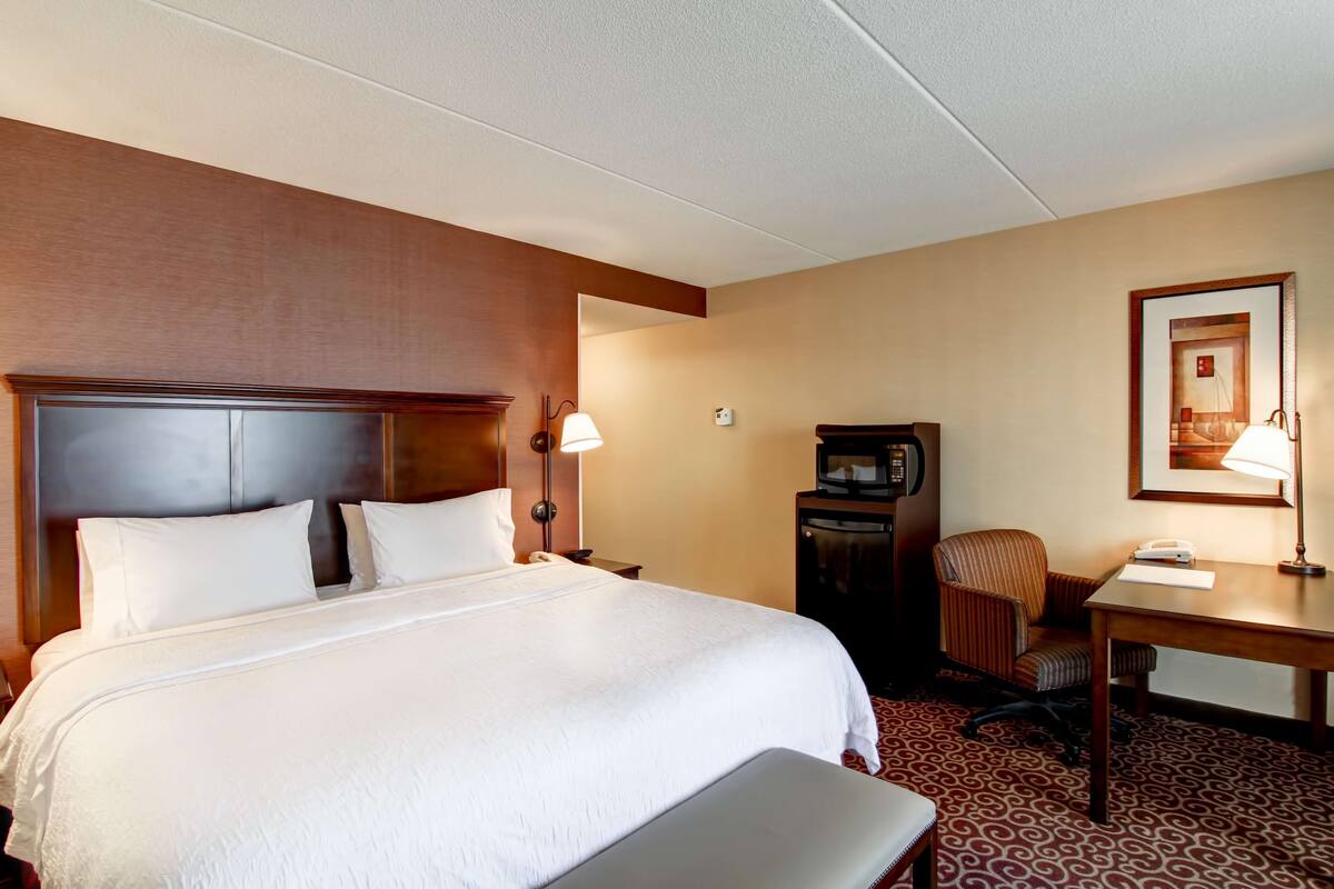 A hotel room with a large bed, a desk with a telephone, a chair, and a television.