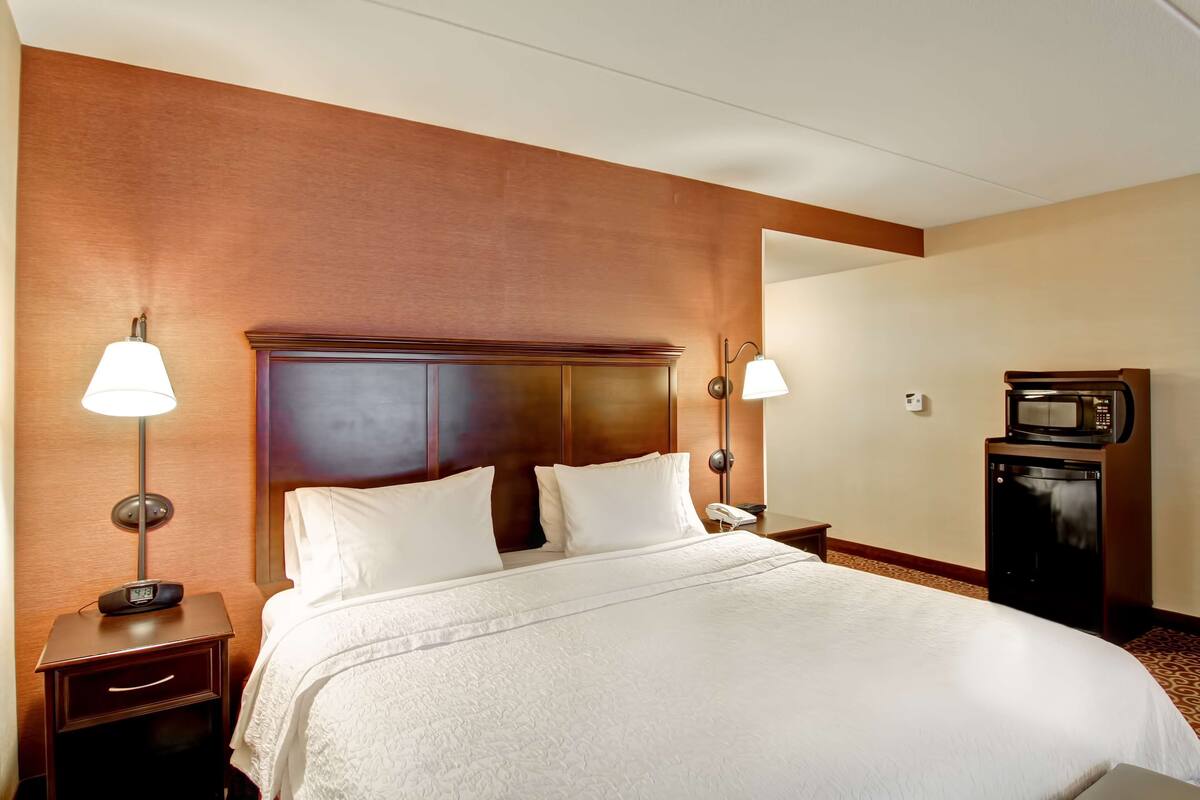 A hotel room with a large bed, two bedside lamps, a nightstand, a microwave, and a telephone.