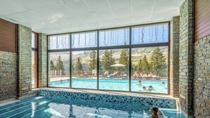 An indoor swimming pool with a view of an outdoor pool area, stone walls, and a clear sky. - Pierre & Vacances Premium Flaine Les Terrasses d'Eos (Araches-la-Frasse)