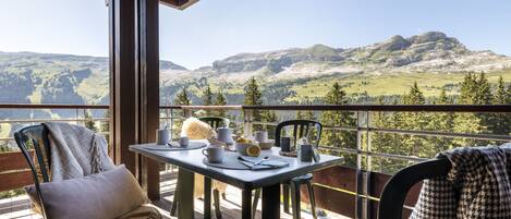 Un balcon avec une table dressée pour deux personnes, offrant une vue sur un paysage montagneux.