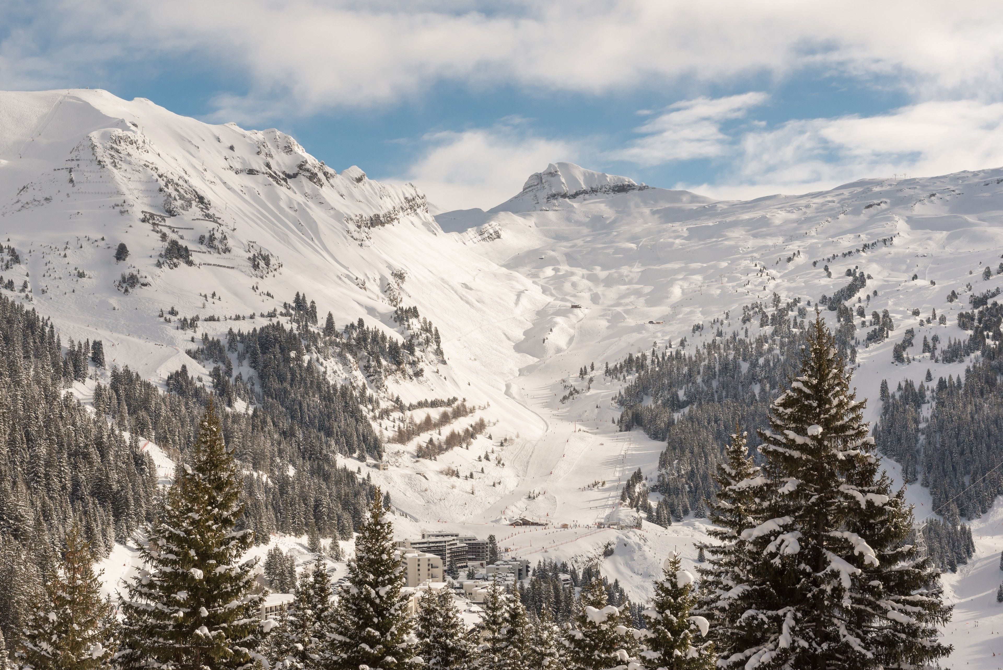 Un paisaje montañoso cubierto de nieve, con una estación de esquí y edificios integrados entre los árboles.