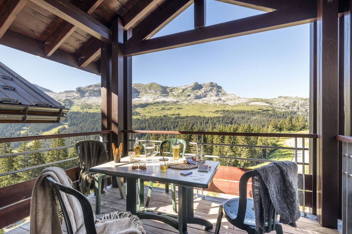 Eine Holzterrasse mit Tisch für Zwei, mit Blick auf eine Berglandschaft.