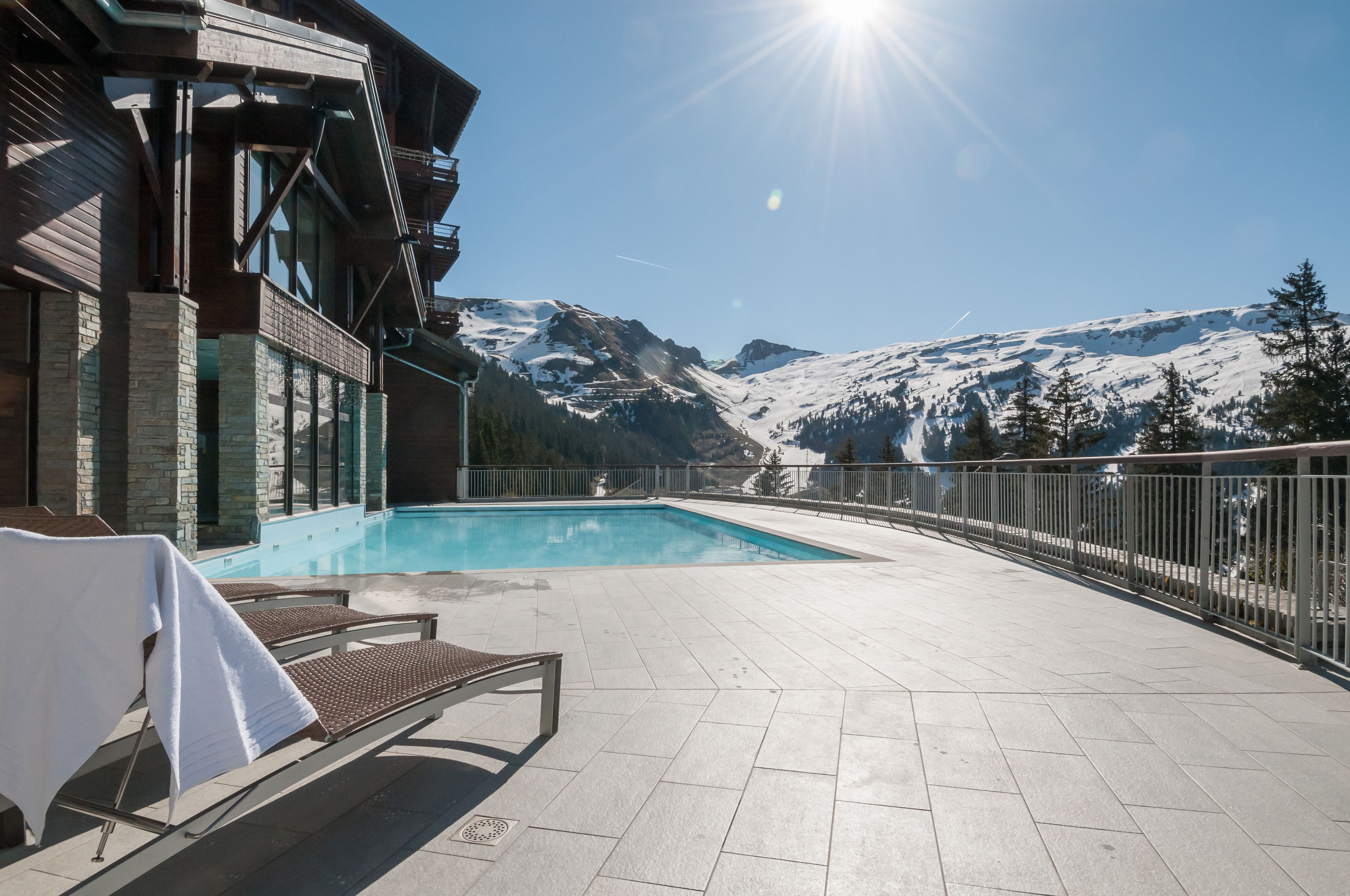 Ein Poolbereich mit Liegestühlen und Blick auf schneebedeckte Berge.