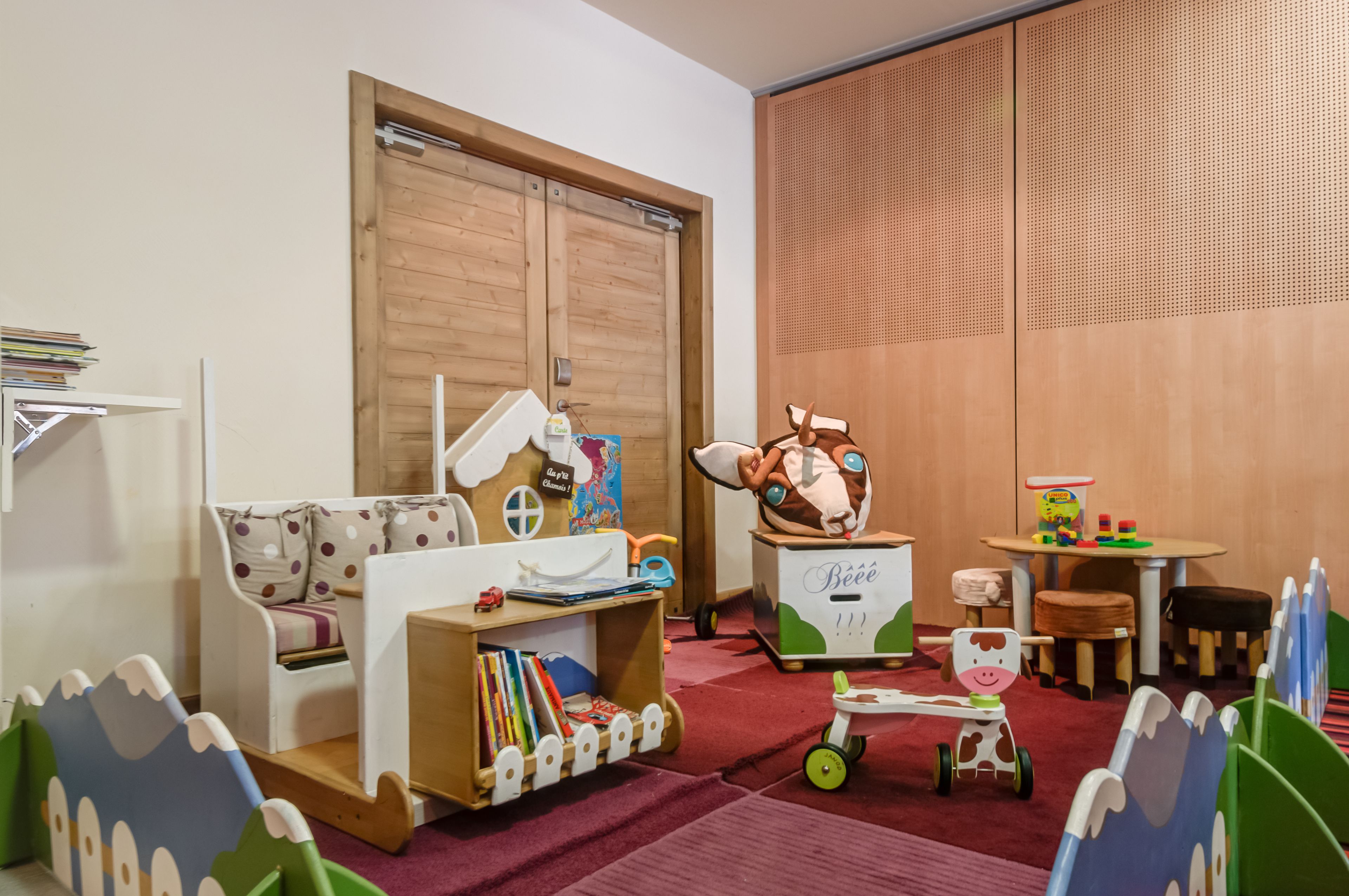Una sala de juegos infantil con un armario de madera, un sofá blanco, una mesita pequeña y un carrito de juguetes.