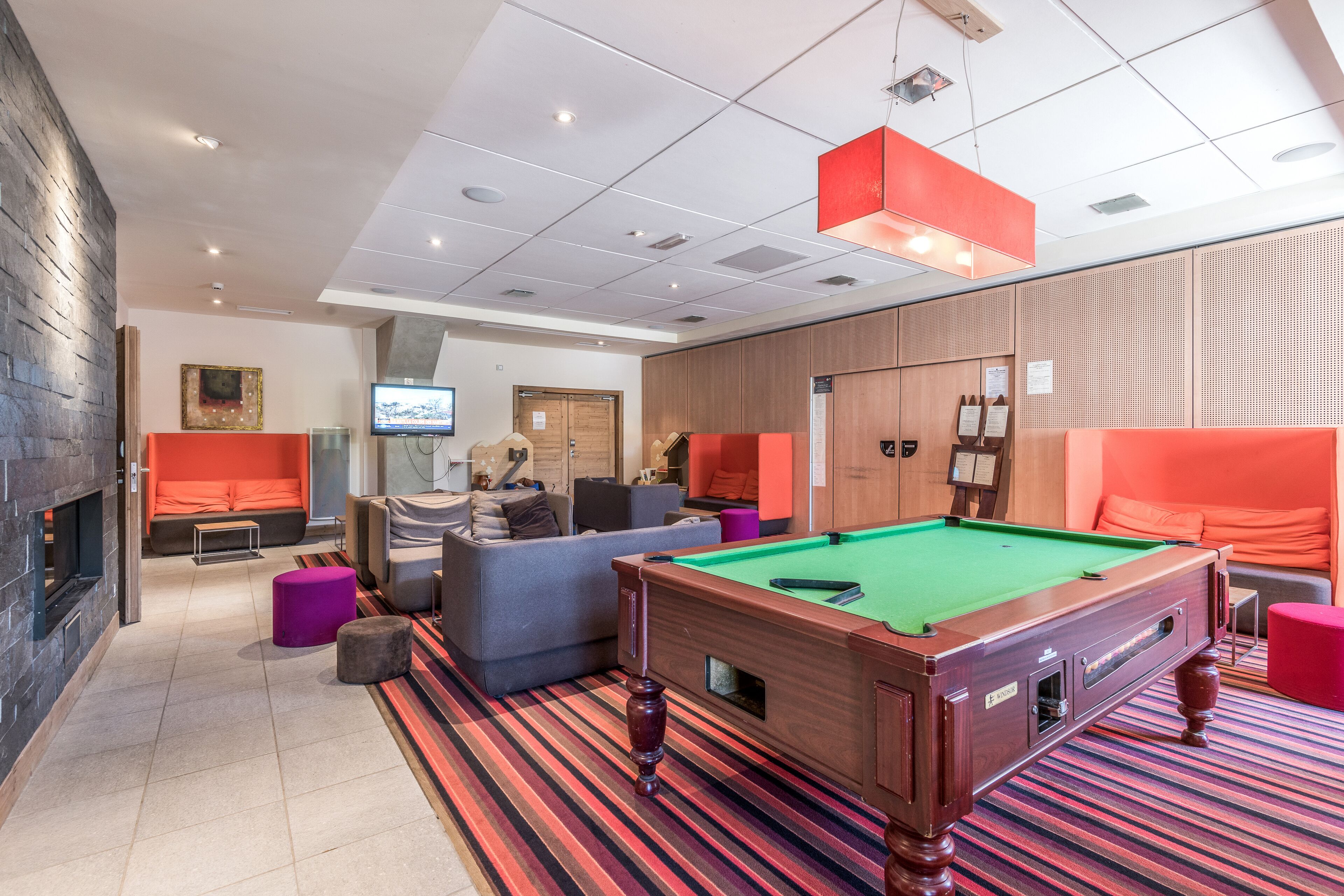 A modern lounge area with a pool table, seating, and a fireplace.