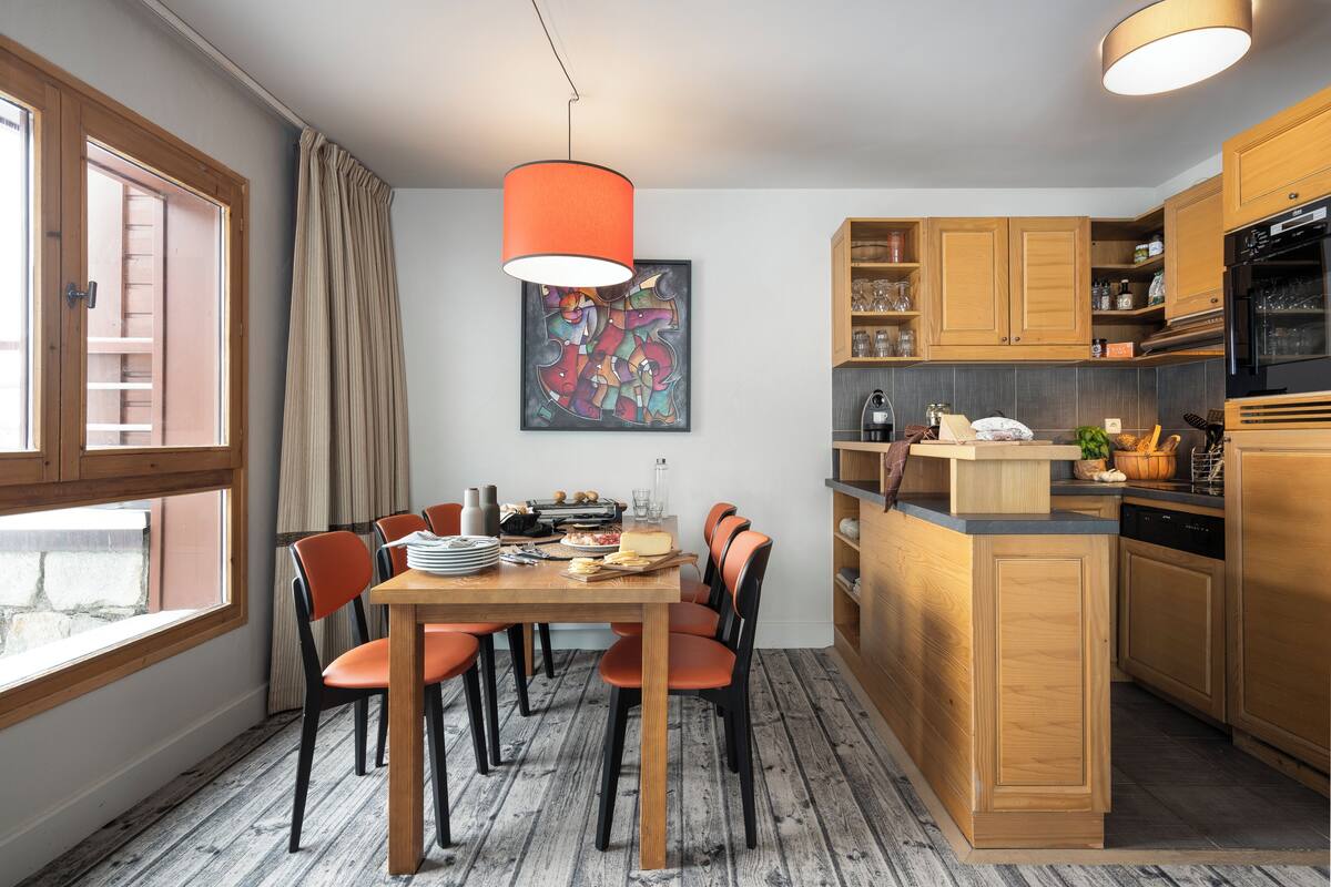 Eine moderne Küche mit Holzausstattung, ein Essbereich mit orangefarbenen Stühlen und ein großes Fenster.
