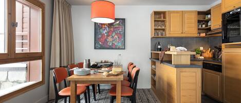 Una cocina moderna con armarios de madera, un comedor con sillas color naranja y un ventanal grande.