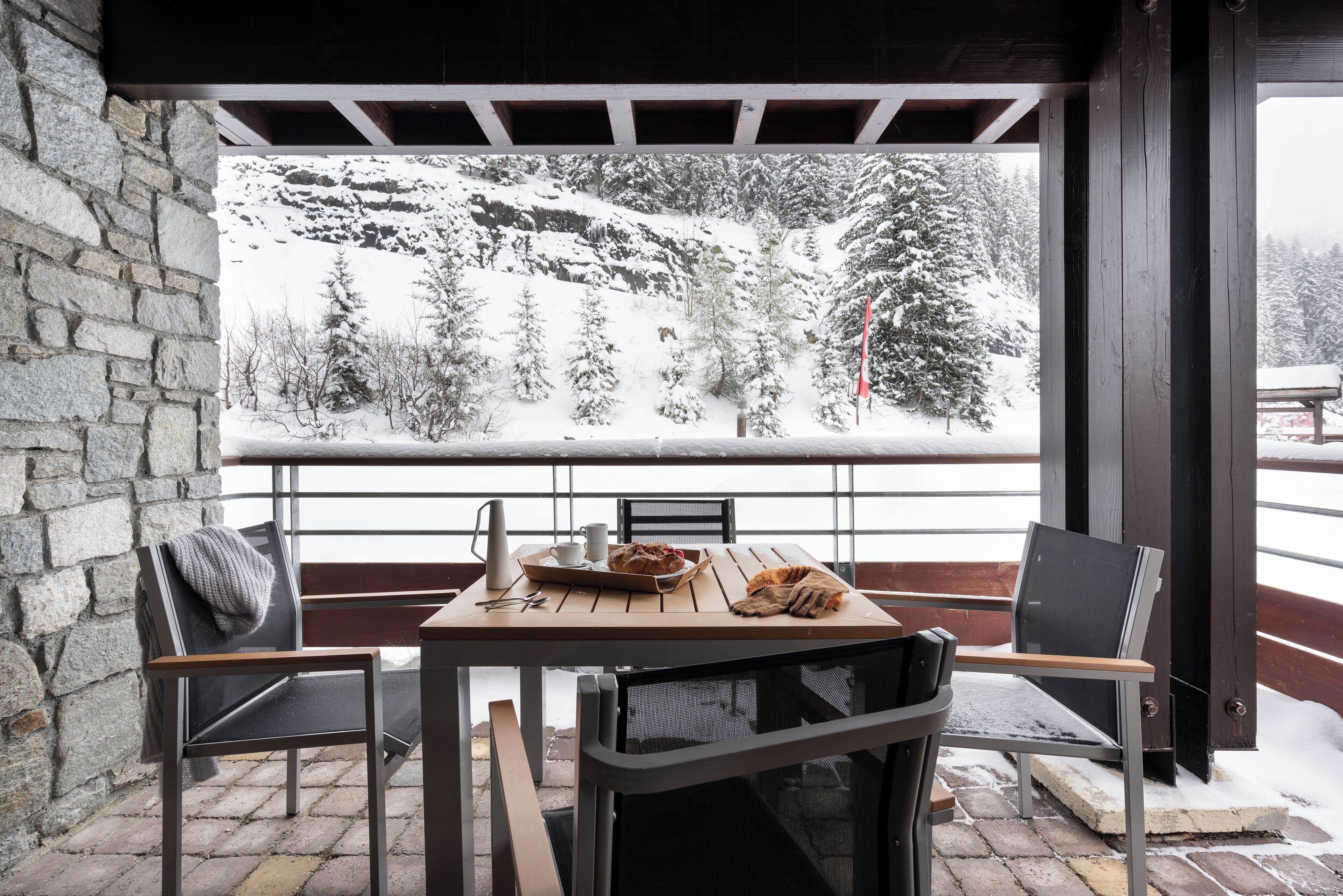 A wooden table with chairs, a bench, and a view of a snowy mountain landscape.