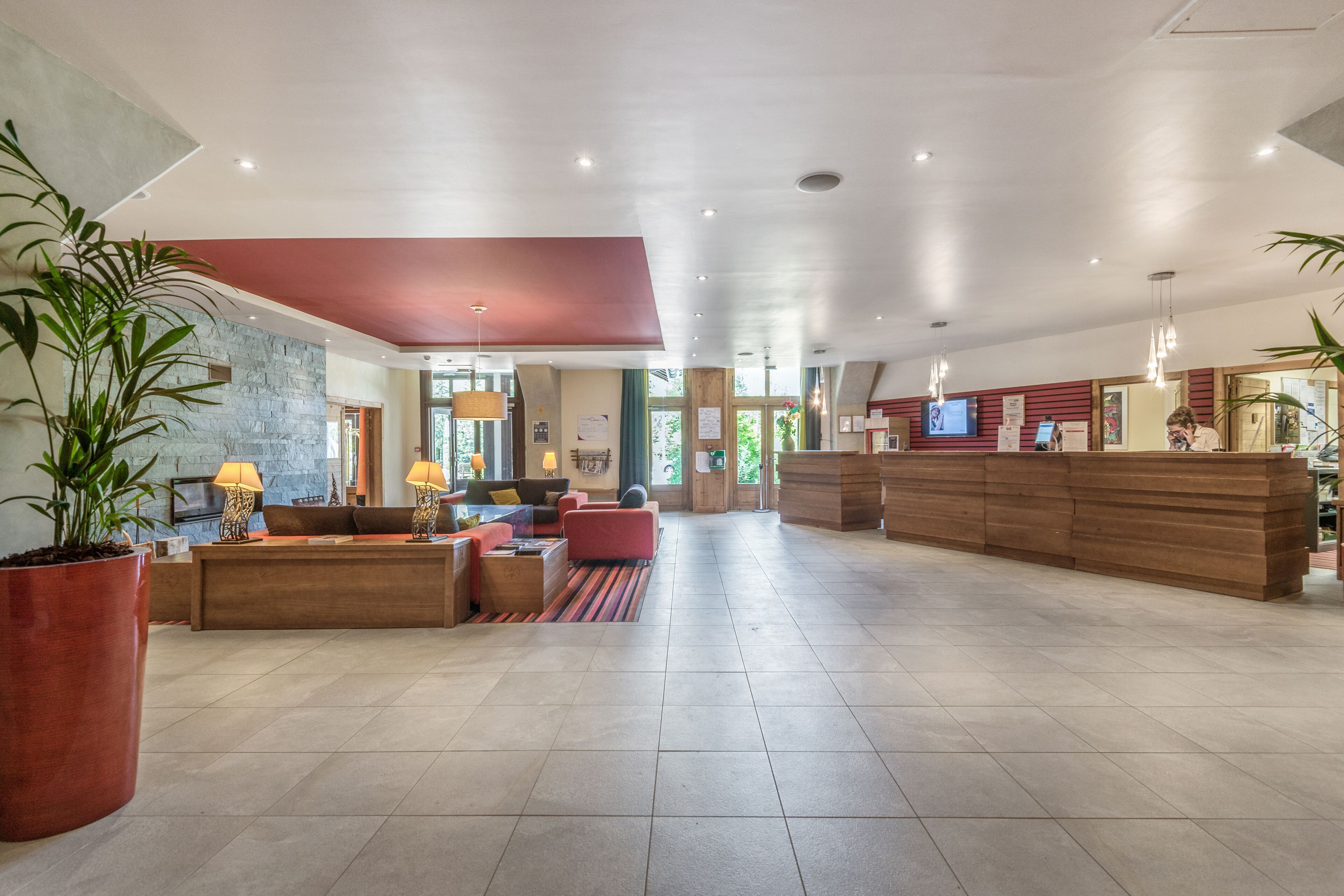 A spacious lobby with a reception desk, seating area, and large potted plants.