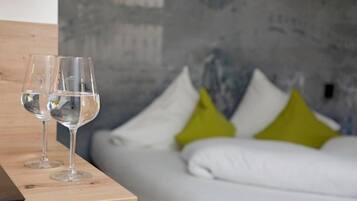 Ein Zimmer mit einem Bett, zwei leere Weingläser auf einem Holztisch und einer grauen, strukturierten Wand.