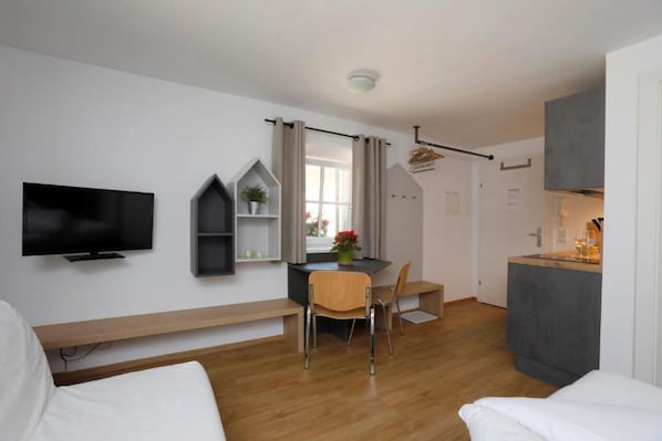 Una habitación moderna con televisión de pantalla plana, una mesa de comedor con sillas, una pequeña cocina y una cama.